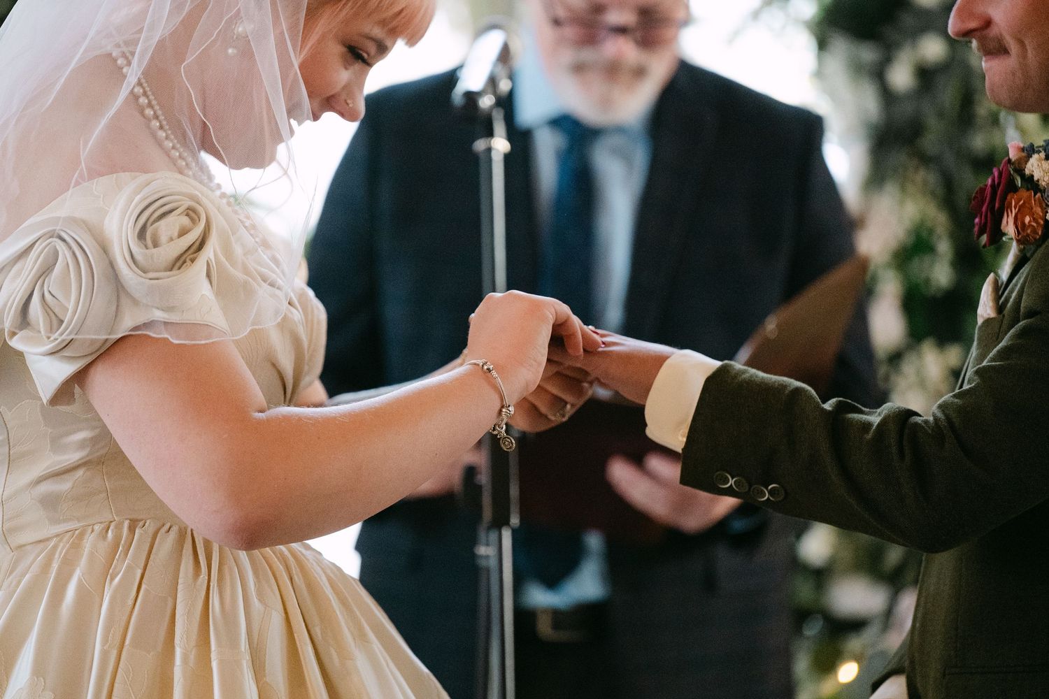 Central MN Wedding Photos | Close-up of bride sliding wedding ring onto groom's finger during ring exchange ceremony.