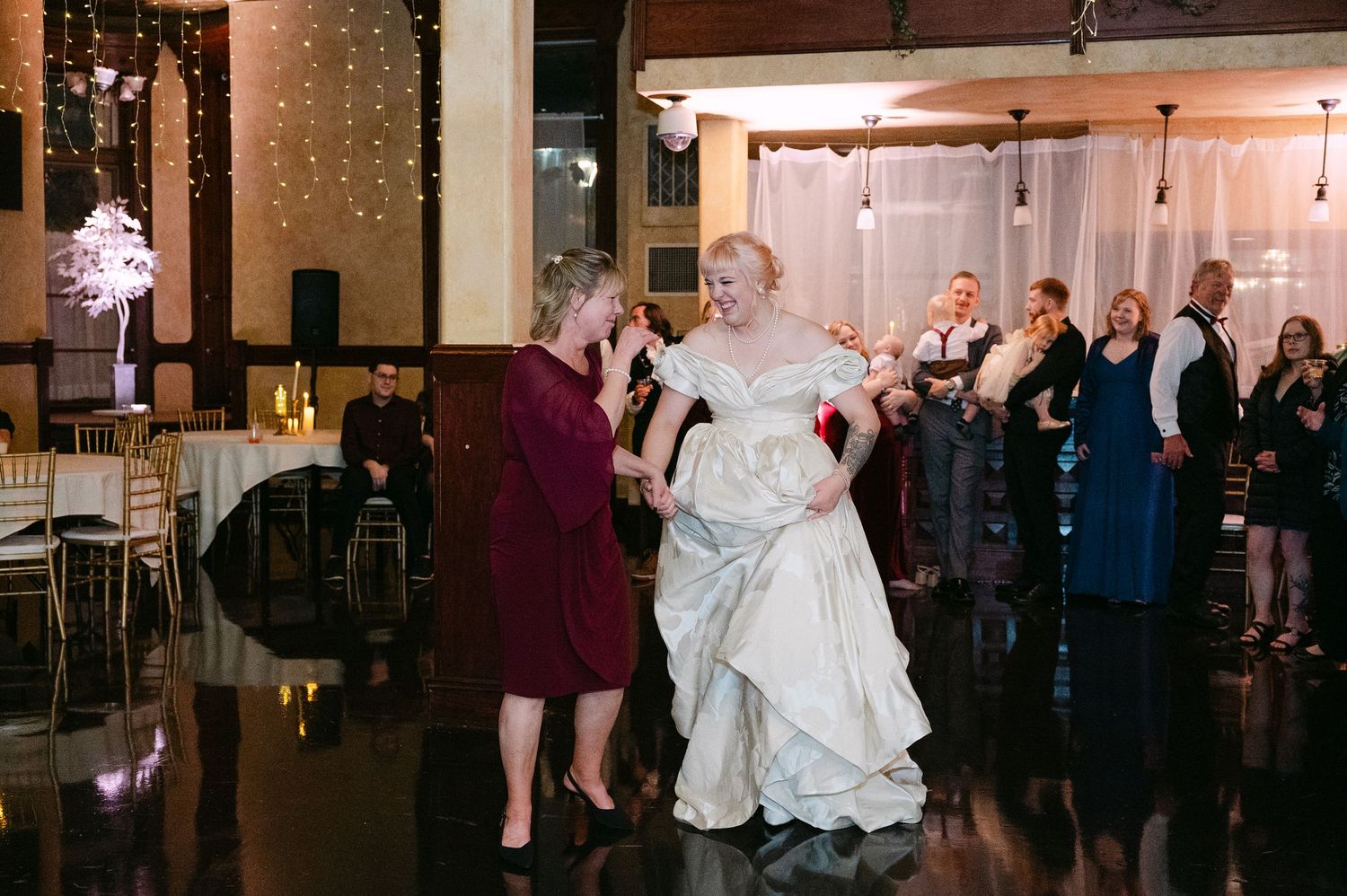 Central MN Wedding Photos | Bride in ivory gown dances with woman in burgundy dress at wedding reception.