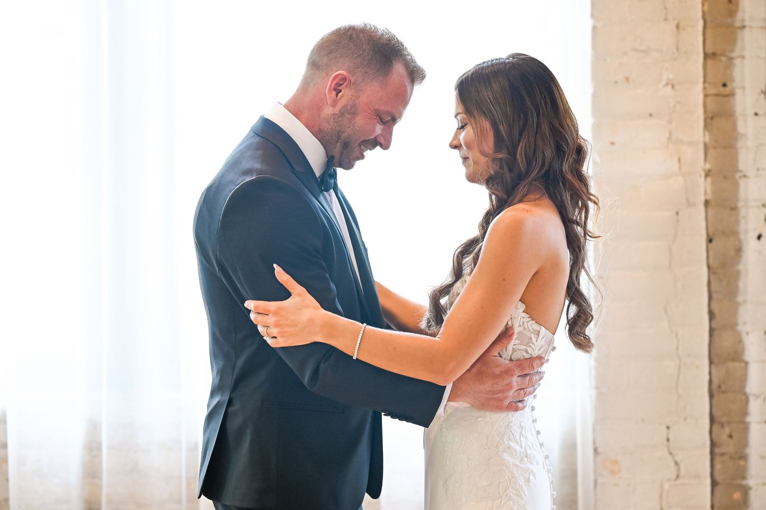 Romantic first look moment between couple in an industrial-style venue with brick walls.