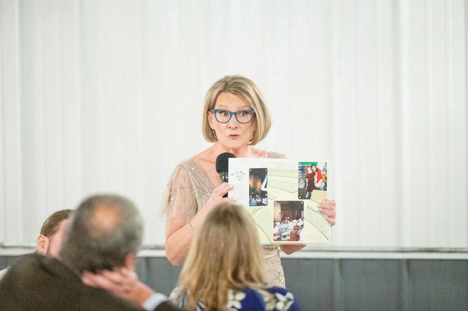 Woman holding photo collage while speaking at a wedding reception with microphone.