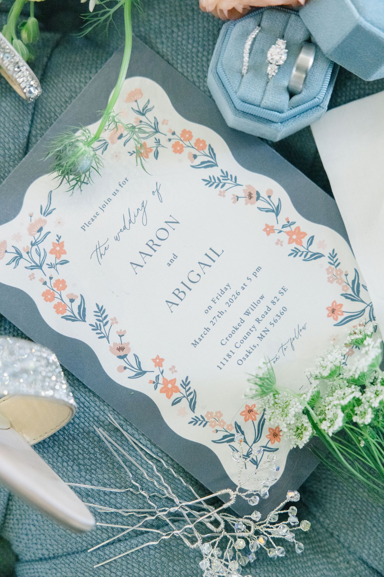 Elegant wedding invitation for Aaron and Abigail with floral border design, displayed with rings and bridal accessories.