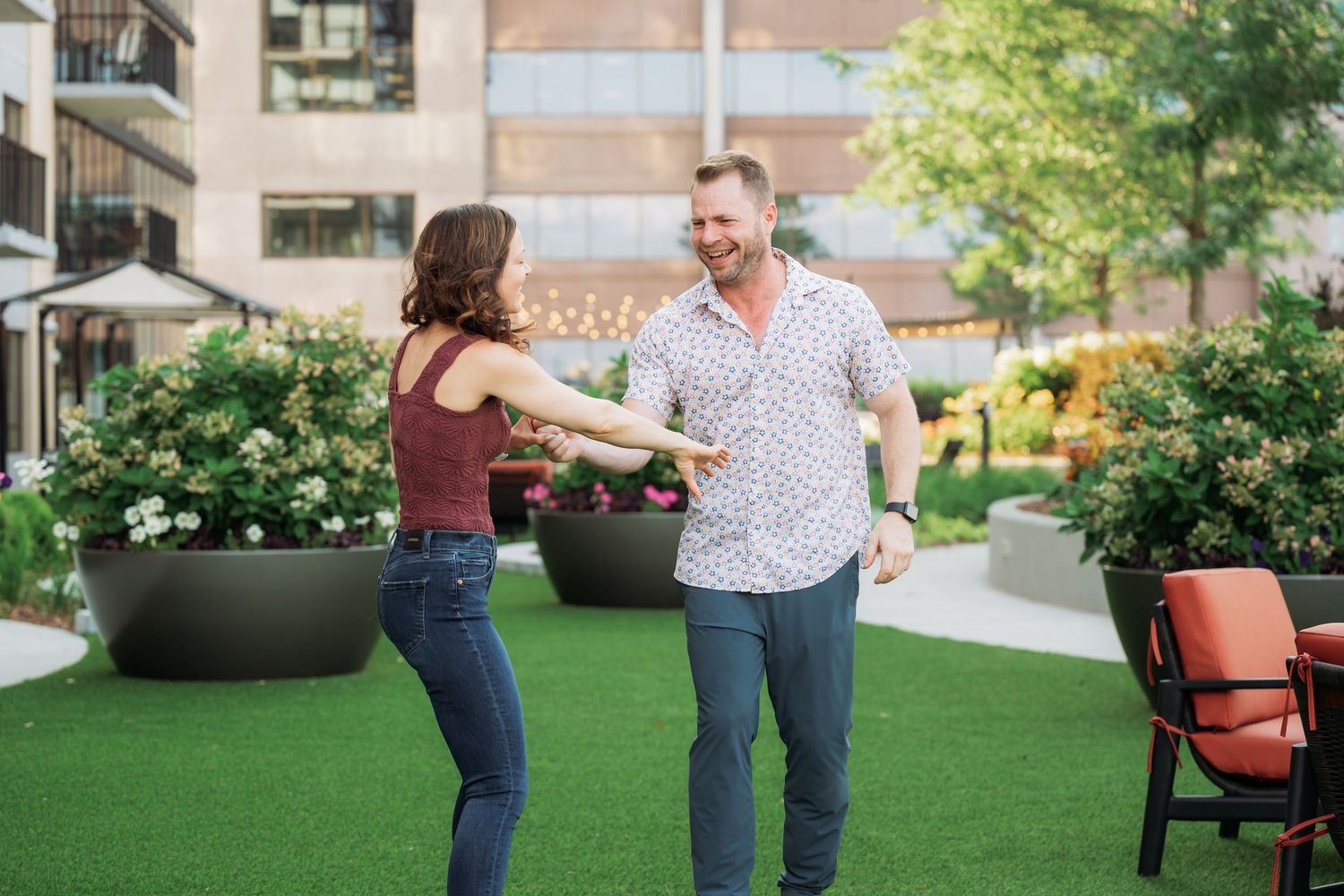 Couple dancing together playfully on a green lawn with modern architecture in the background.