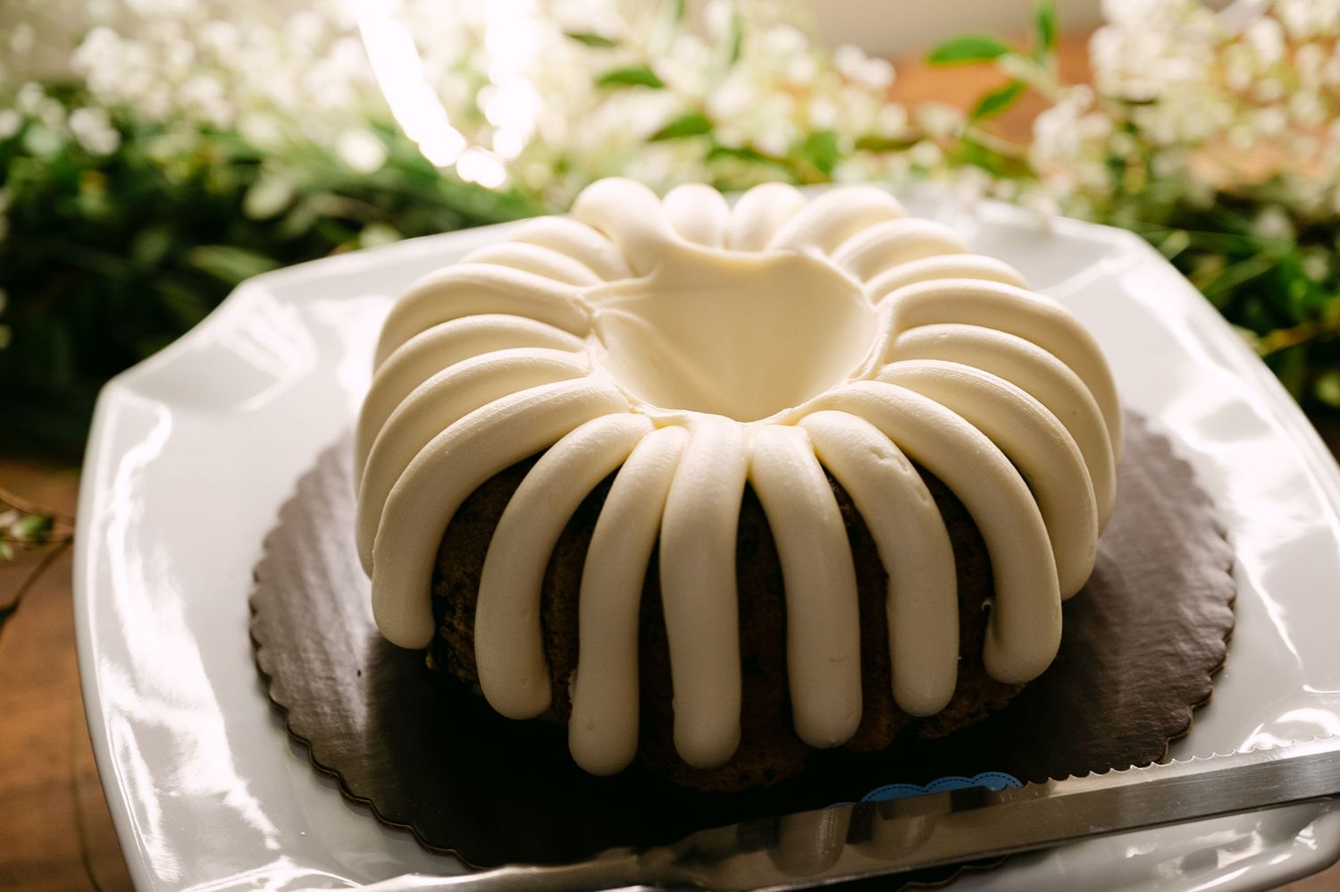 White-frosted chocolate bundt cake displayed on a white plate with floral decorations.