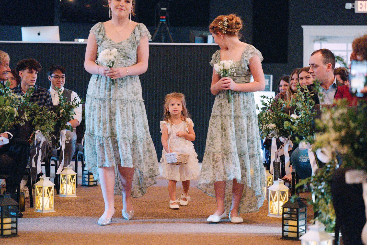 Bridesmaids in light blue floral dresses and a young flower girl stand at the altar during a wedding ceremony.