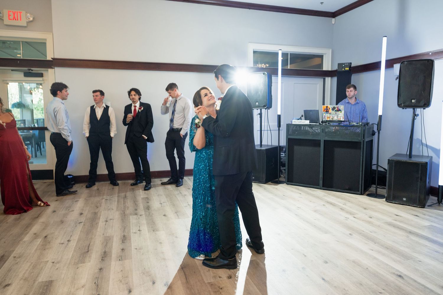 Couple shares first dance at wedding reception as guests watch and DJ plays music in background.