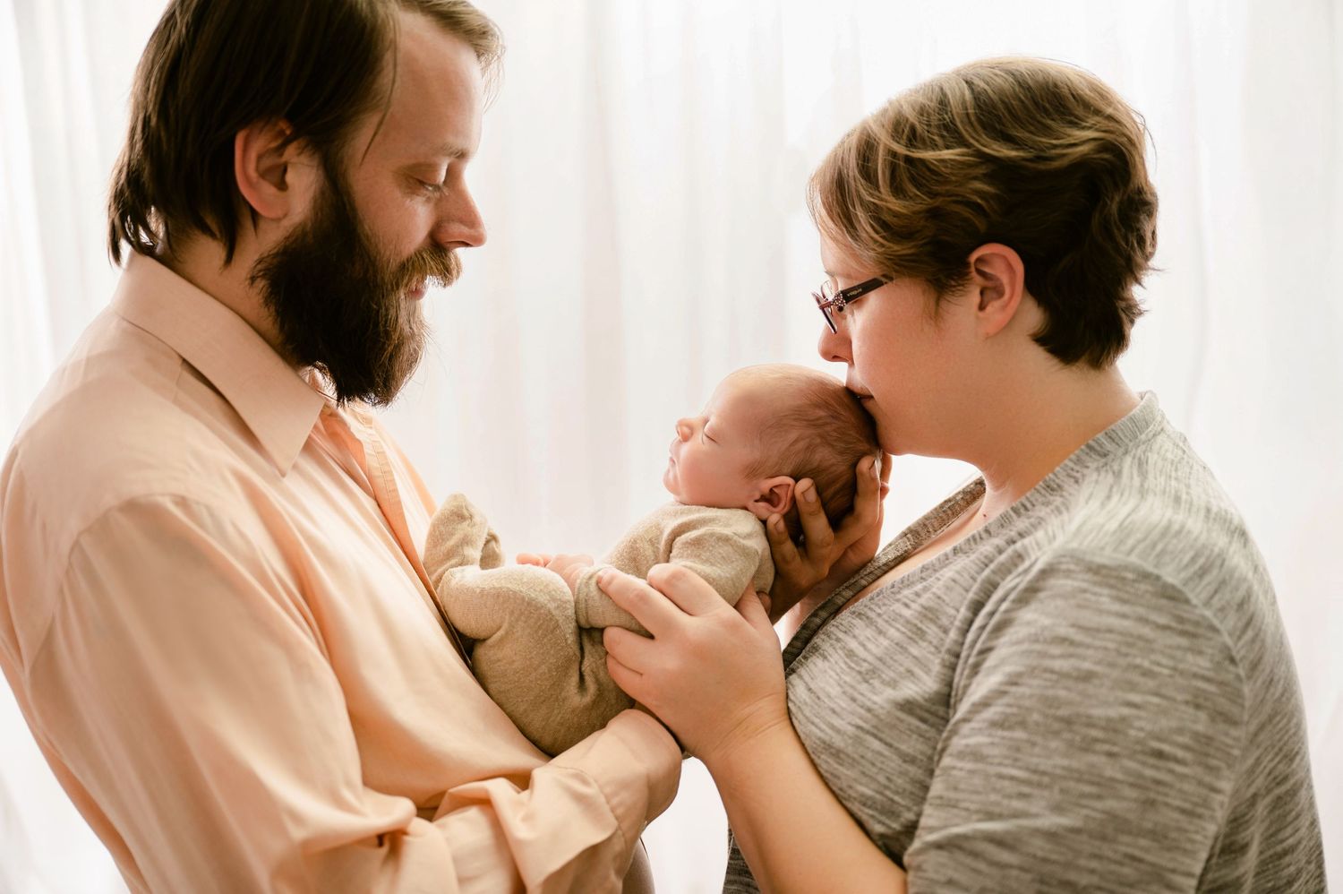 Parents tenderly hold and gaze at their newborn baby in an intimate family moment at home.