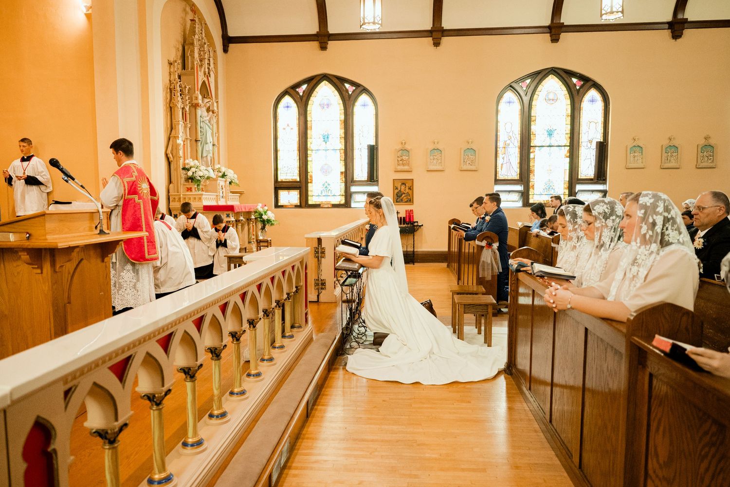 A wedding ceremony taking place inside a church with arched windows and wooden railings.