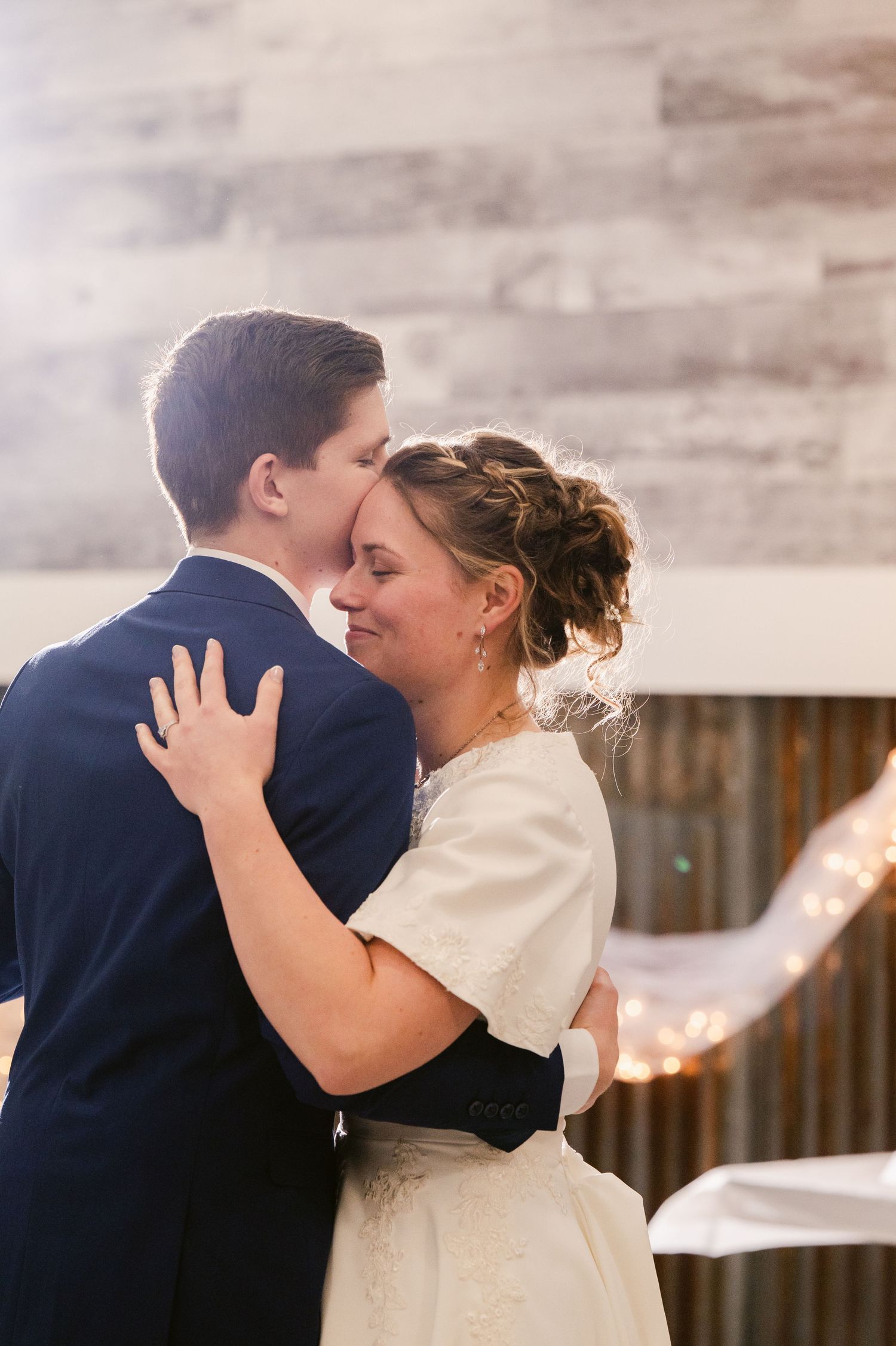 Romantic wedding couple sharing tender kisses against a rustic background.