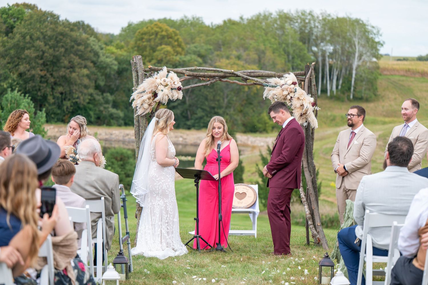 Outdoor wedding ceremony setup with white chairs and floral arch in a scenic meadow landscape.