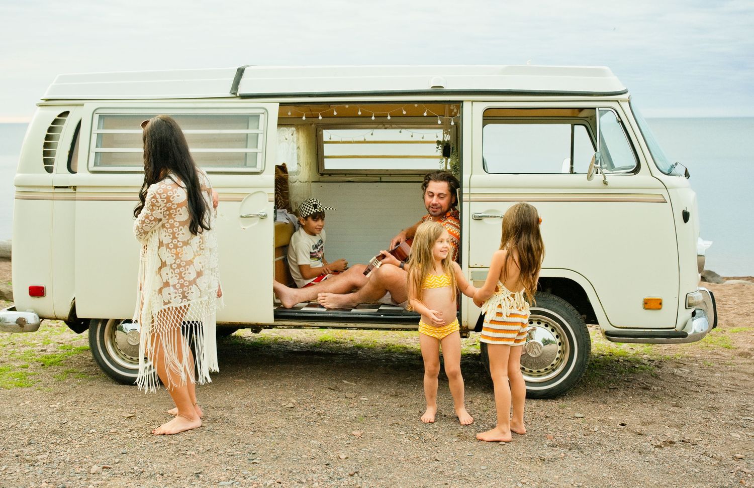 Family enjoying a beach trip with a vintage VW camper van, children playing outside while dad relaxes inside.