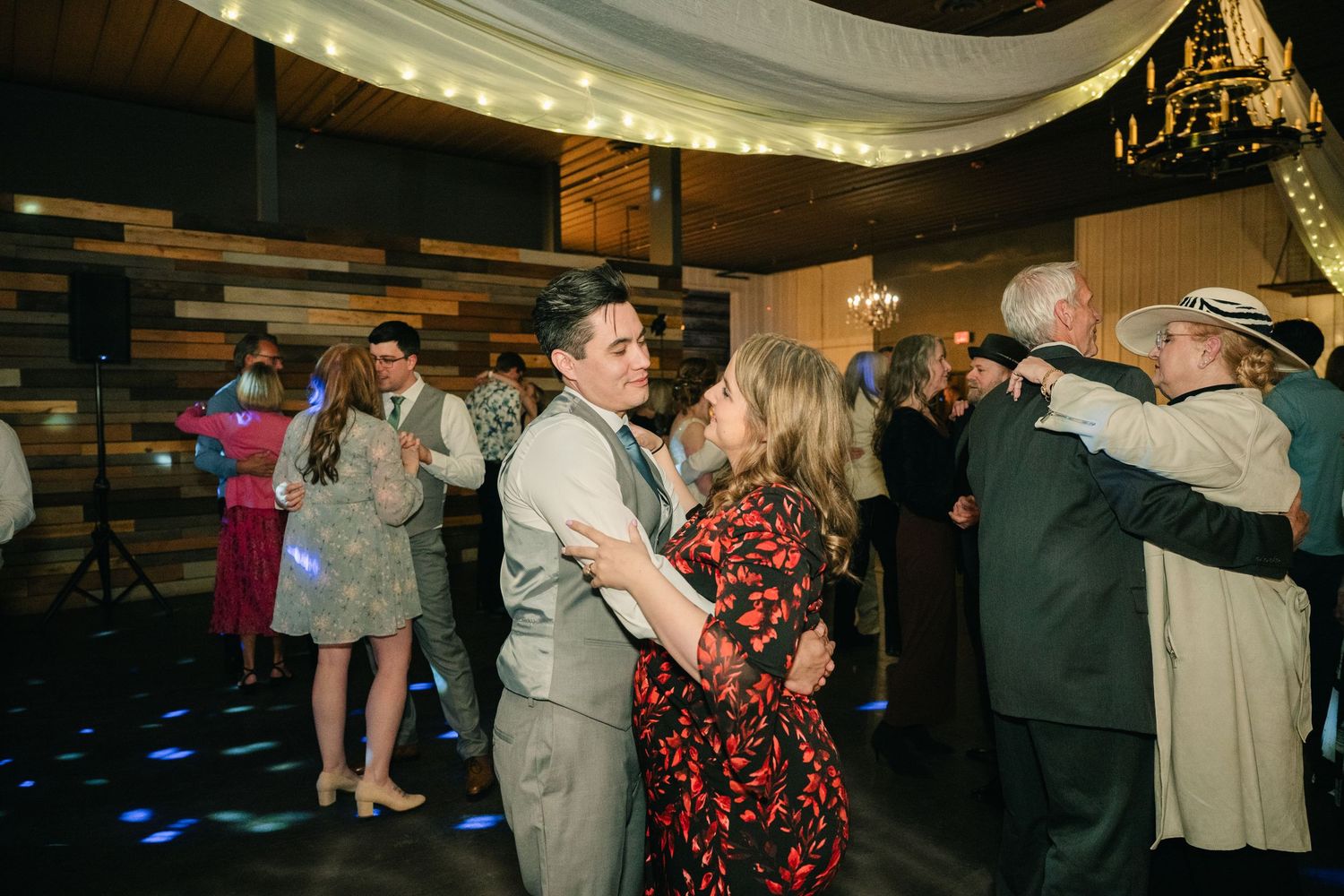 Guests dance together joyfully on illuminated dance floor during lively wedding reception celebration.