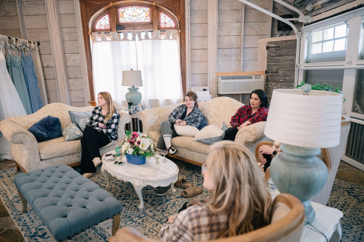 Women gather in a cozy rustic living room with vintage sofas, blue accents, and warm wood walls for a casual meeting.
