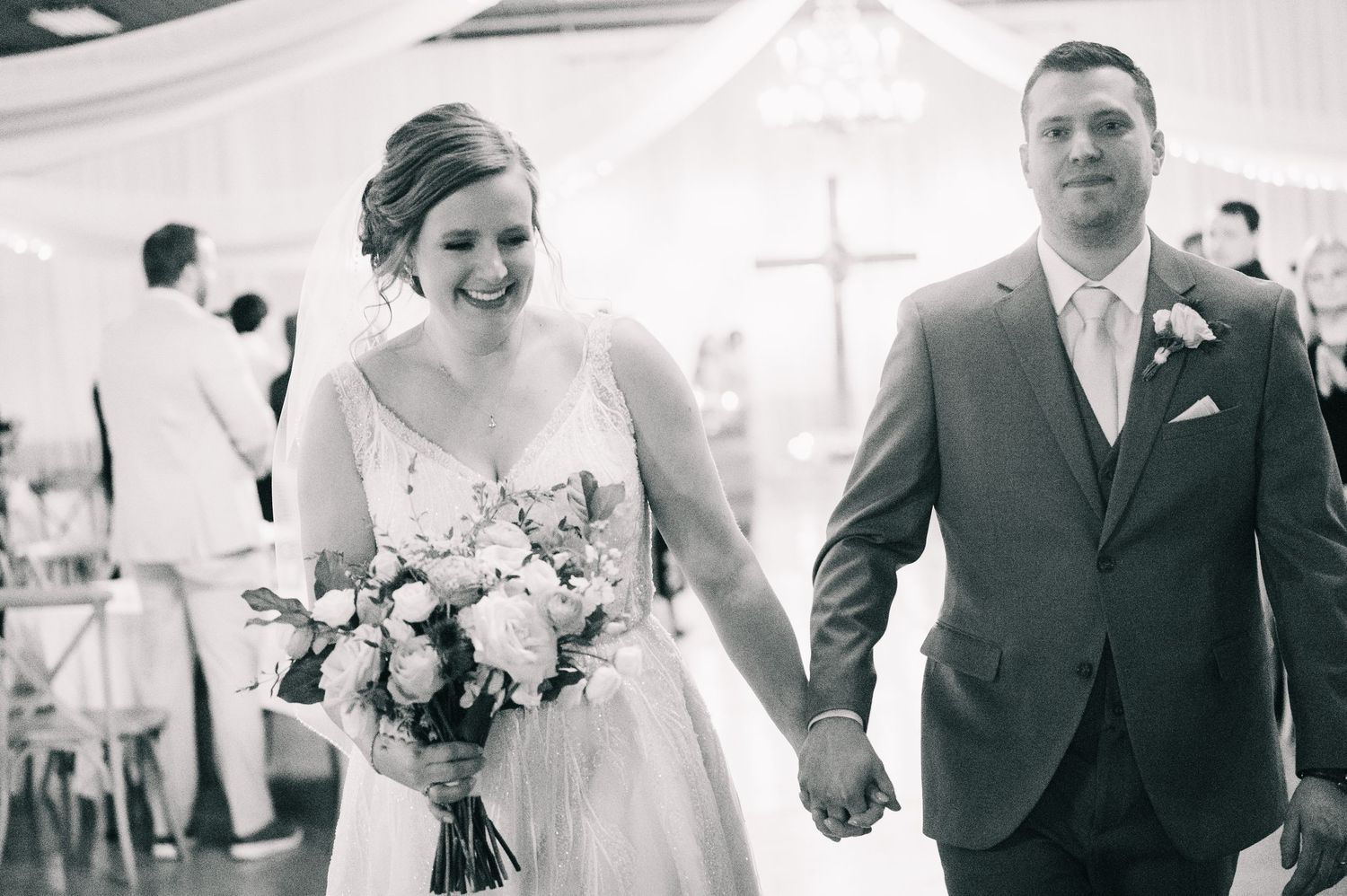 Black and white photo of a joyful bride and groom walking hand in hand after their wedding ceremony.