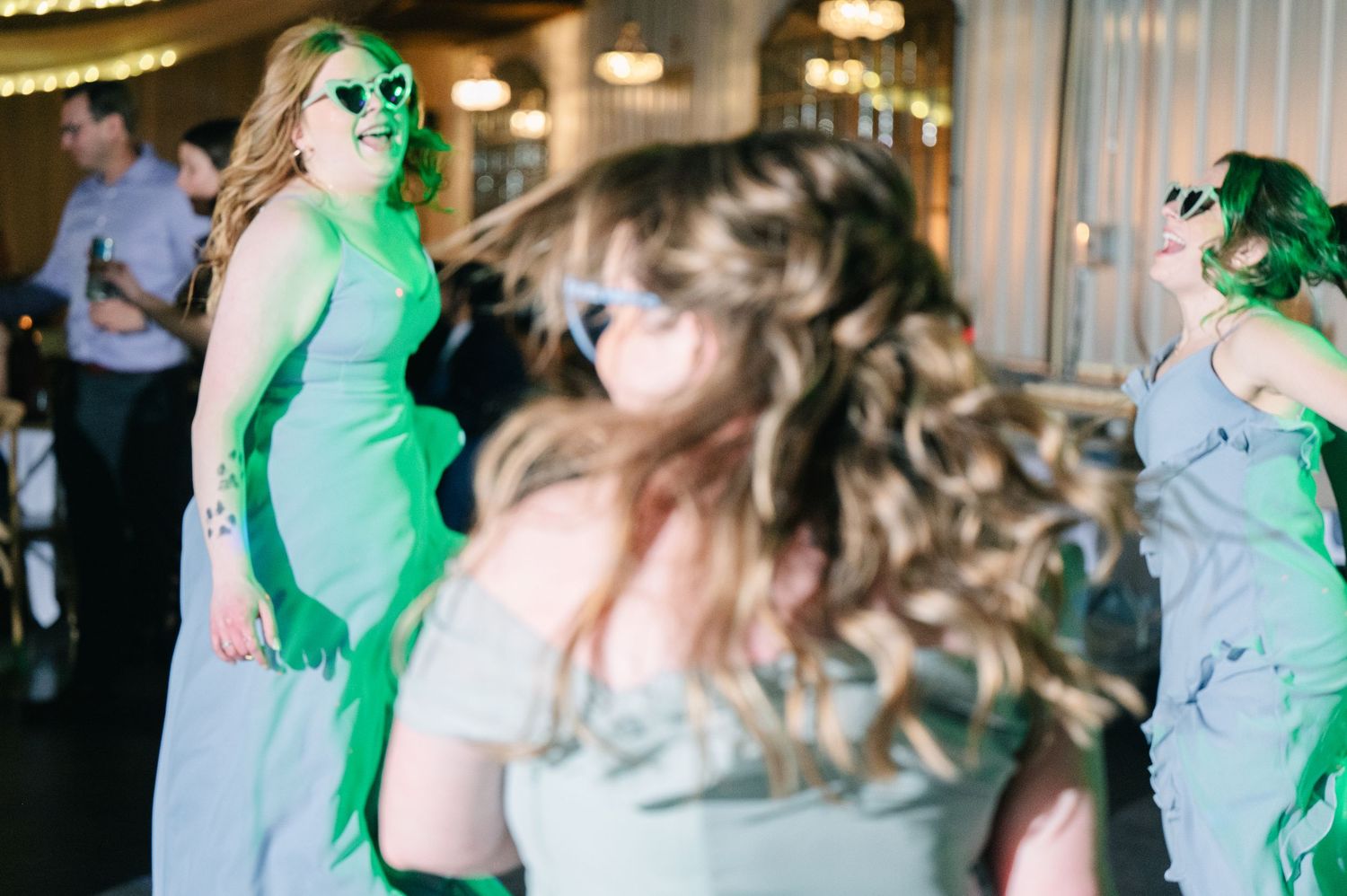Bridesmaids dance energetically under green lights on the wedding reception dance floor.