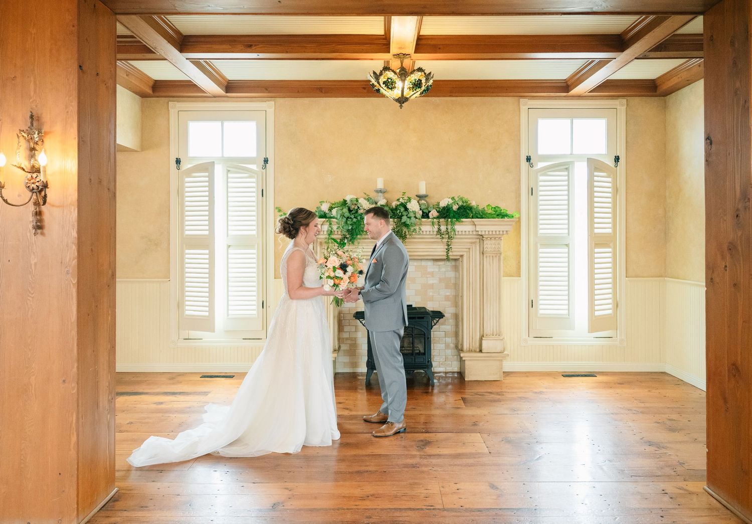 Bride and groom share a first look in an elegant venue with hardwood floors and a floral fireplace.