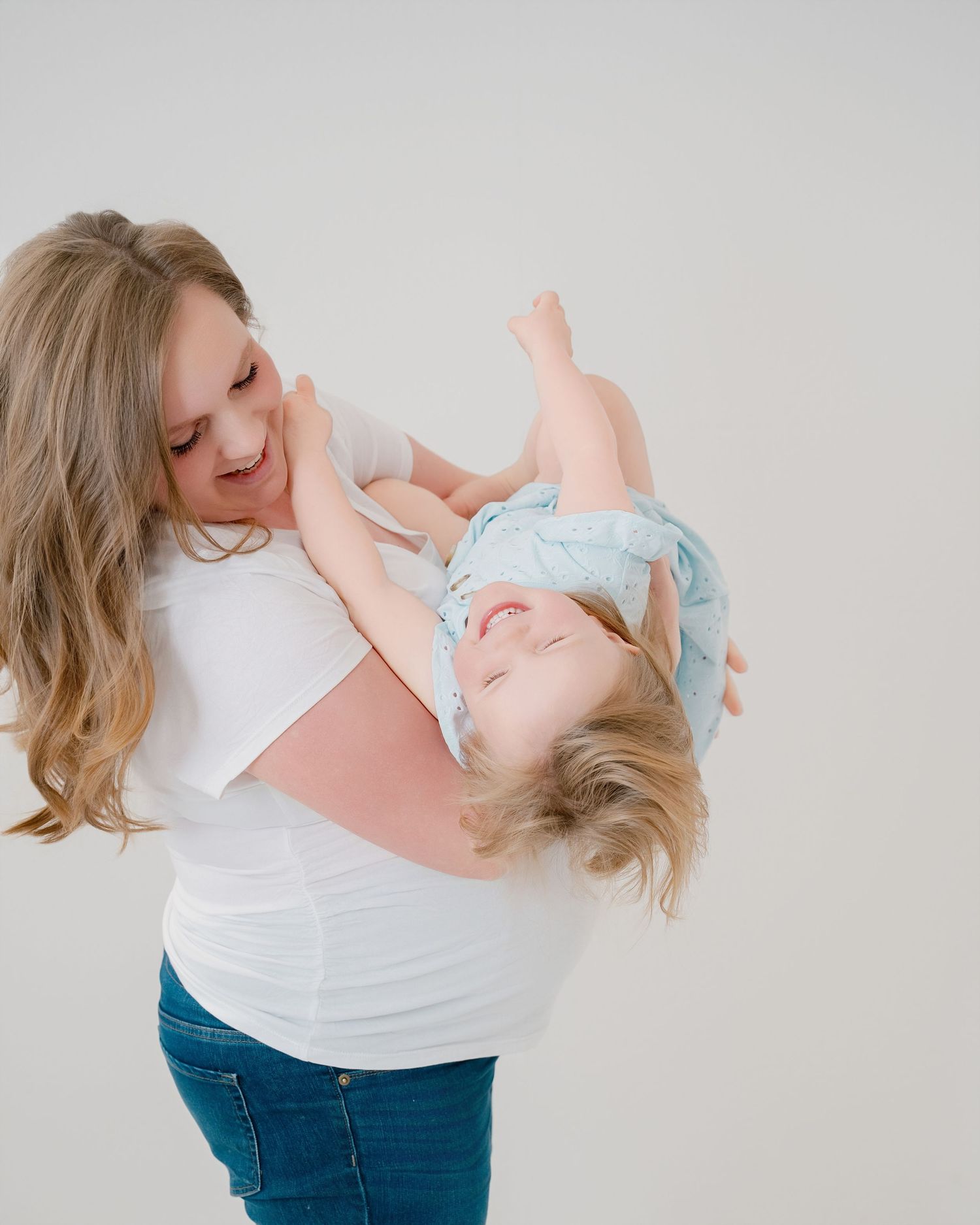 Two parents lean together while embracing their young child in a series of tender poses against a white backdrop.