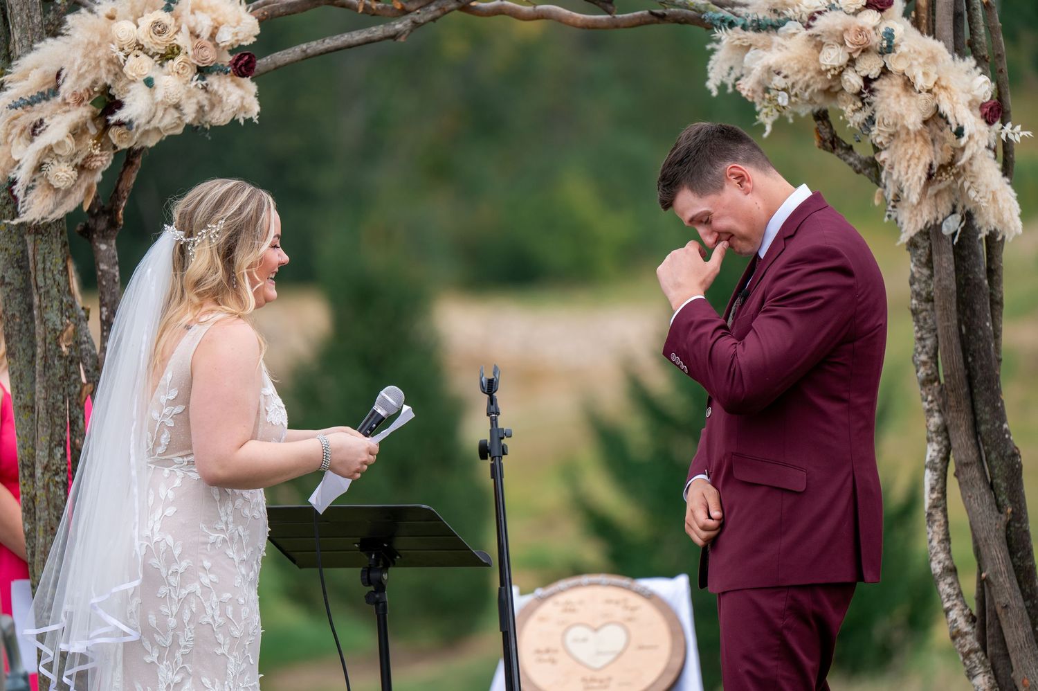 A couple sharing an emotional moment during their wedding vows under a floral-decorated arch.