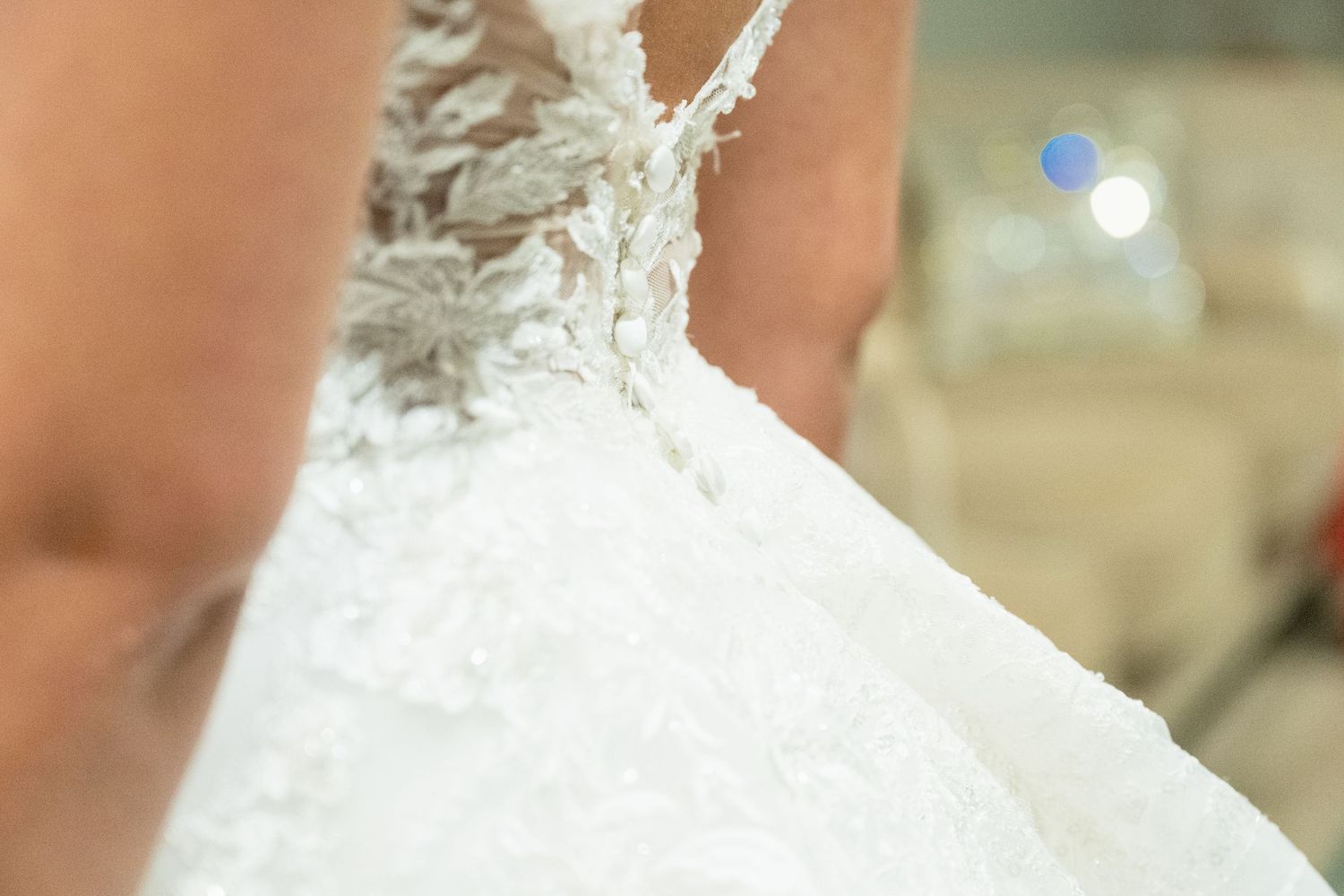 Close-up of an elegant white lace wedding dress with intricate floral embroidery details.