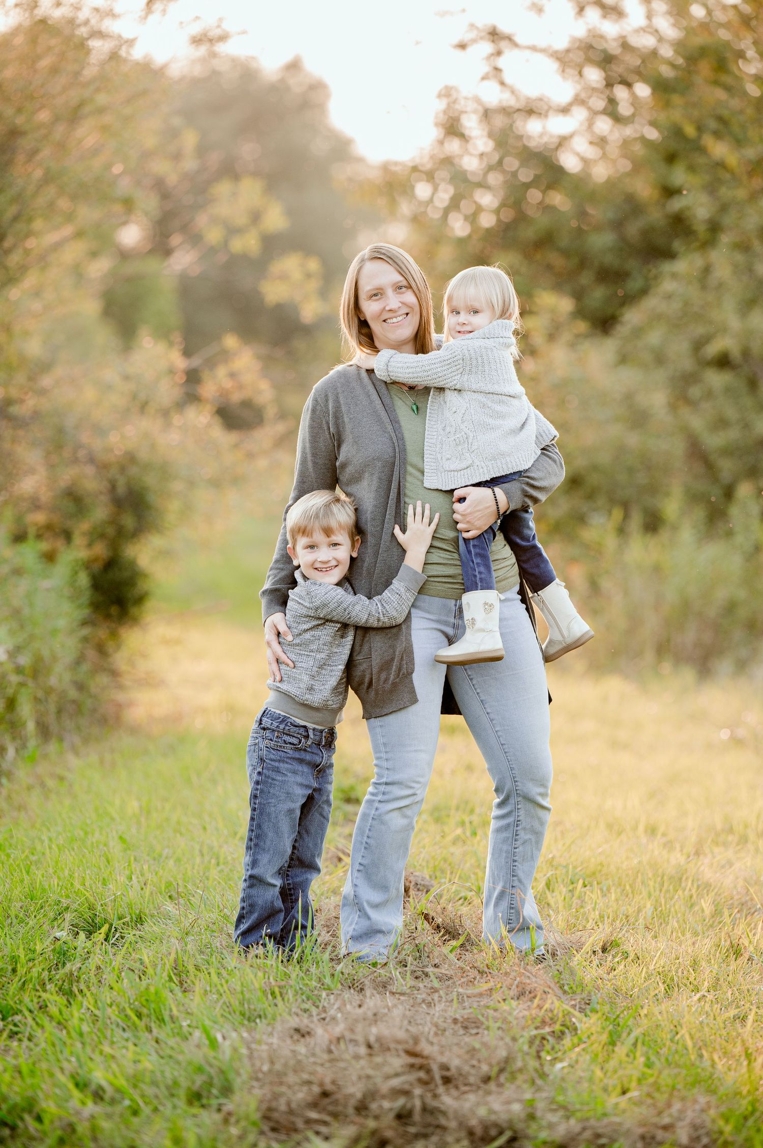Mother and two children pose together in a golden sunlit field during autumn.