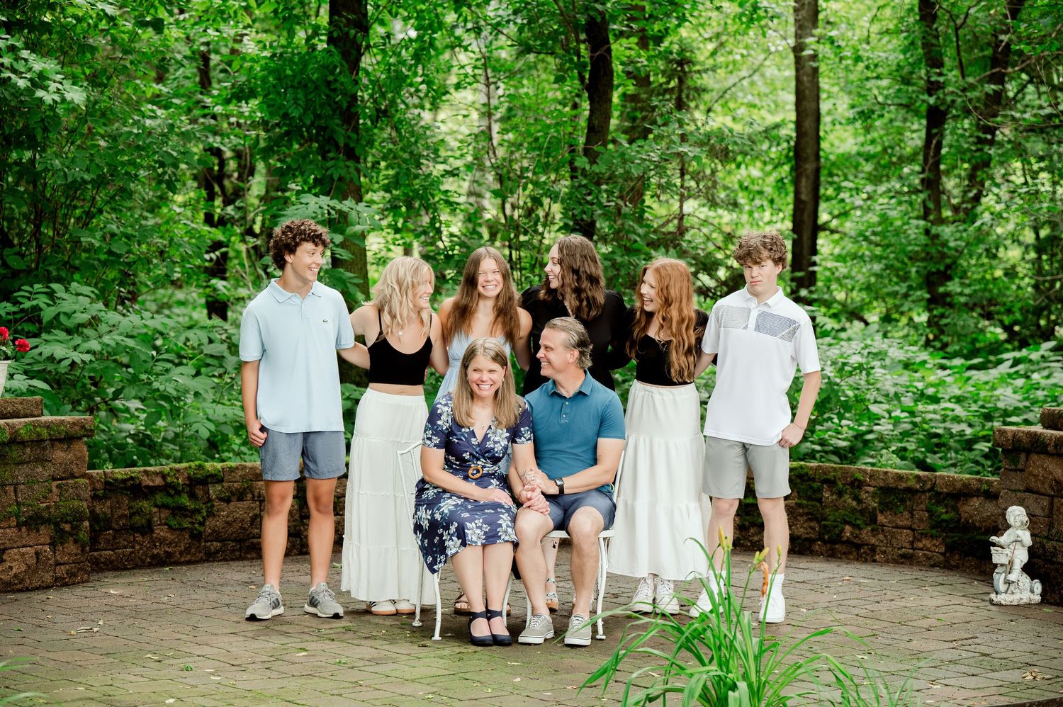 A group photo of family members sitting and standing on a stone patio surrounded by green forest.