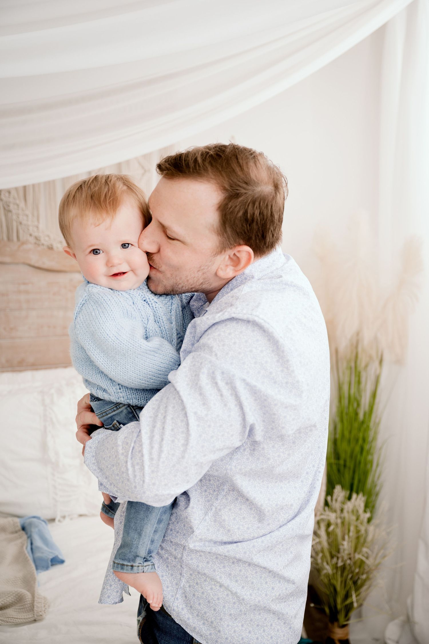 Central MN Milestone Photography - Father kissing his baby on the cheek while holding them in a bright white decorated room.