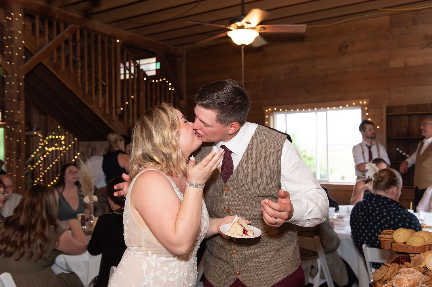 Central MN Wedding Photography - Bride and groom share a kiss while cutting wedding cake at rustic barn reception venue.