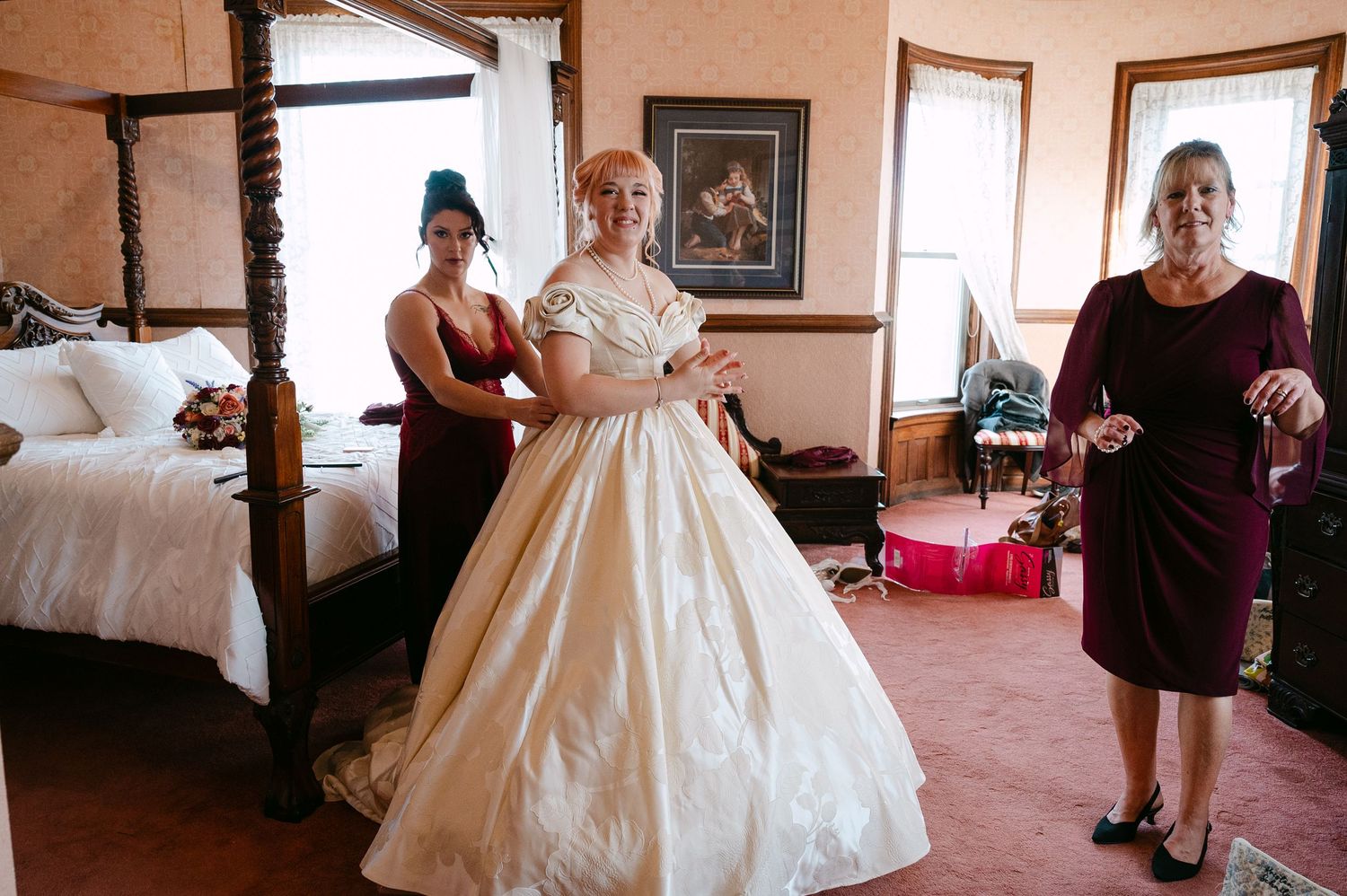 Central MN Wedding Photos | Bride in a white ballgown wedding dress being helped by bridesmaids in a vintage bedroom.