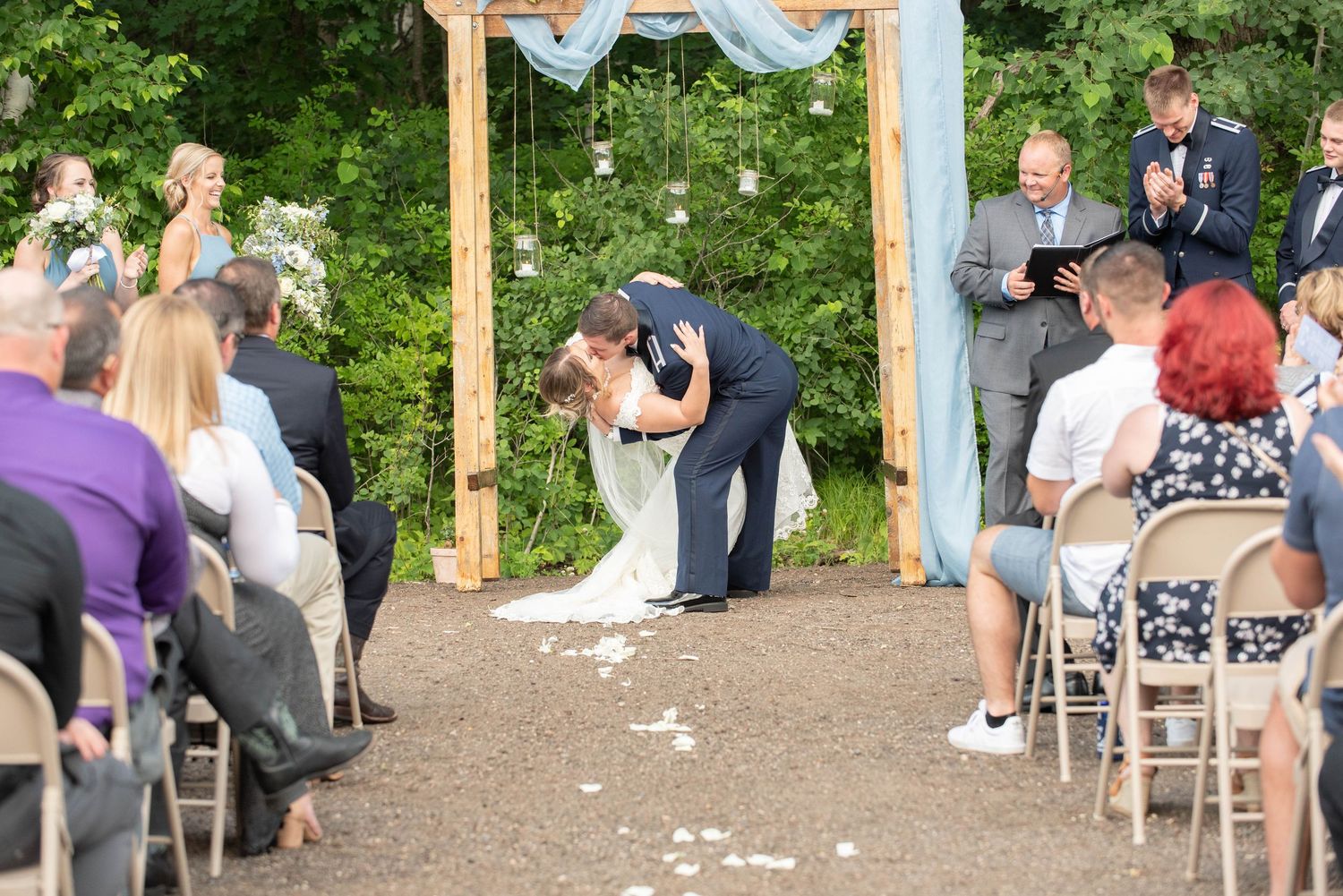 Outdoor wedding ceremony under wooden arch decorated with light blue fabric and white floral accents. Zimmerman MN Weddings