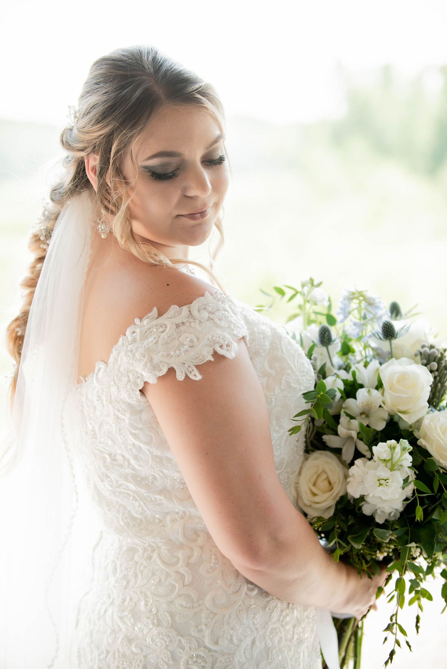 Wedding bouquet of white roses and greenery held by person wearing detailed lace gown with off-shoulder design. Zimmerman MN Weddings
