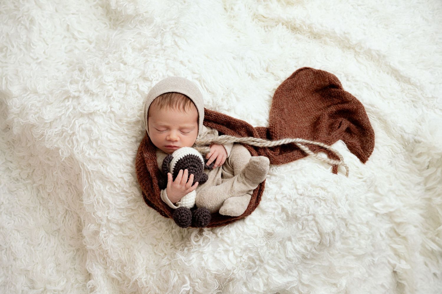 Minnesota Best newborn photographer - A newborn baby lies peacefully in a curled up fetal position on a soft white blanket.
