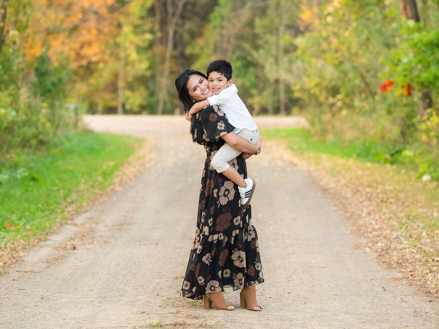 A couple in autumn attire shares a romantic moment on a tree-lined path with golden fall foliage.