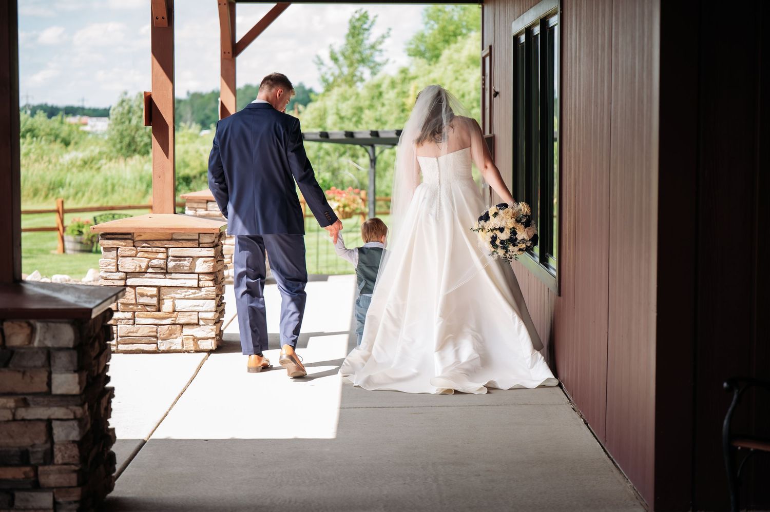 A wedding couple stands in a rustic outdoor venue with wooden beams and stone pillars during their celebration. Pease Minnesota Wedding at N