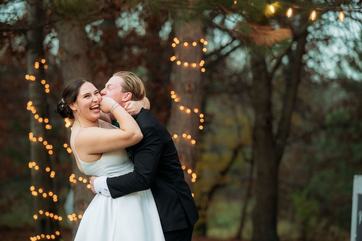 A romantic moment between newlyweds dancing outdoors with twinkling lights in background.