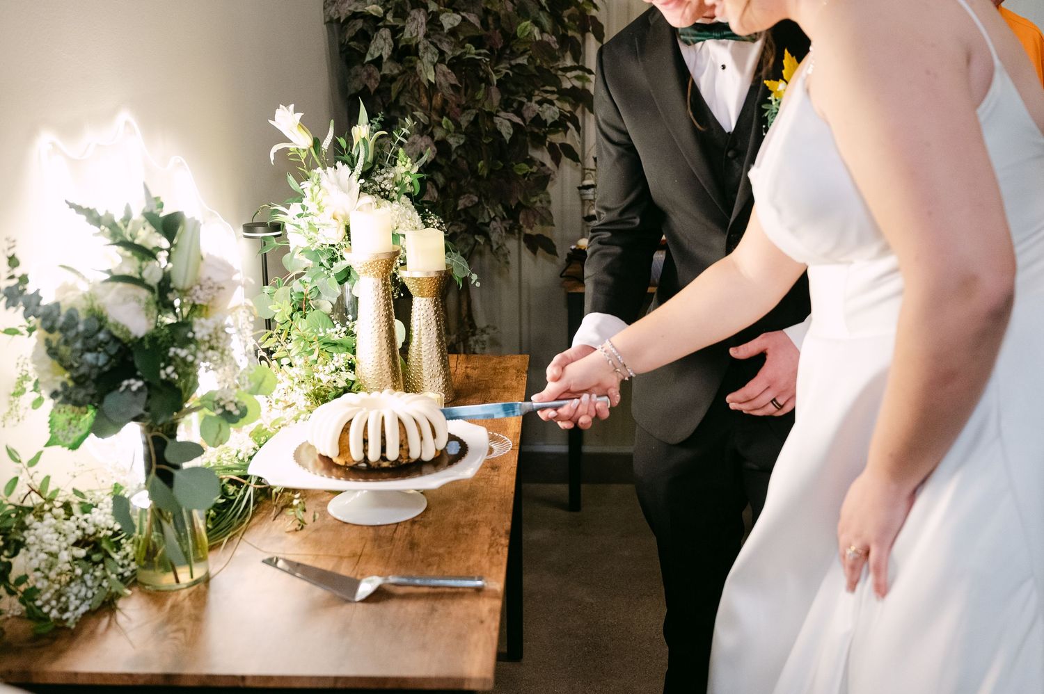 Hands pouring coffee into a white ceramic mug on a rustic wooden table with greenery in the background.