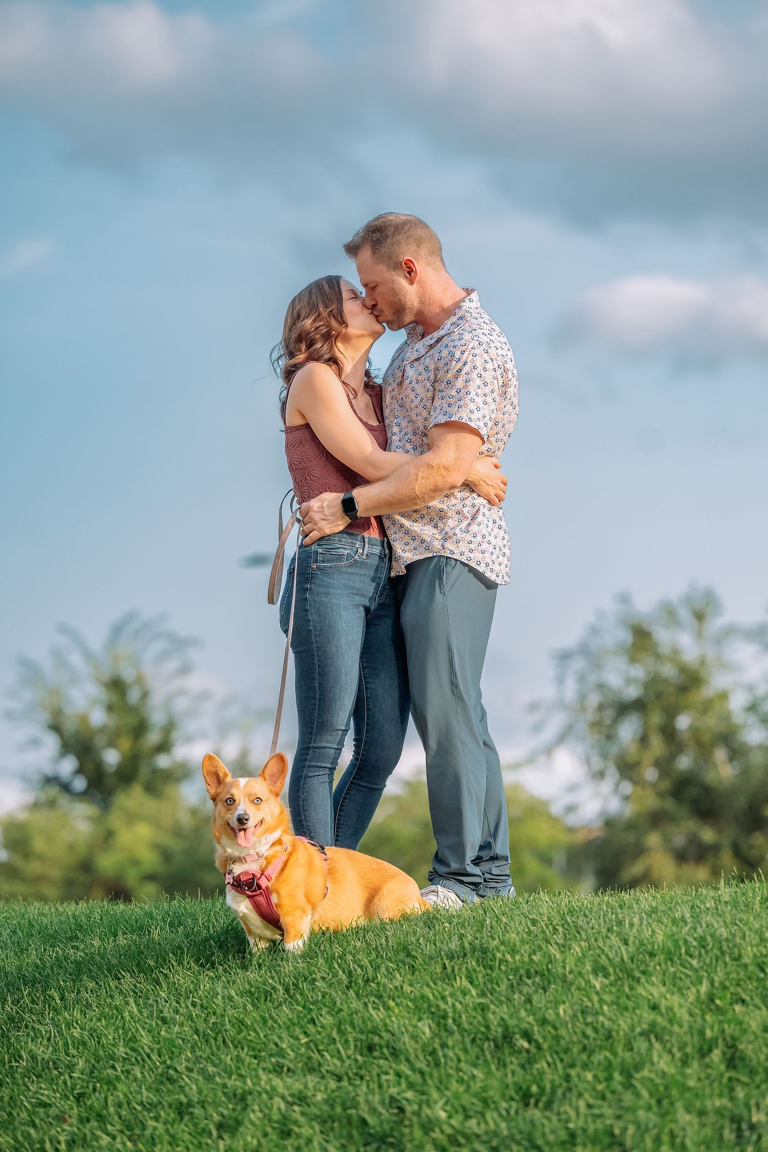 Engagement Photos Minnesota. couple shares romantic moments on a grassy hill while their corgi dog sits nearby watching.