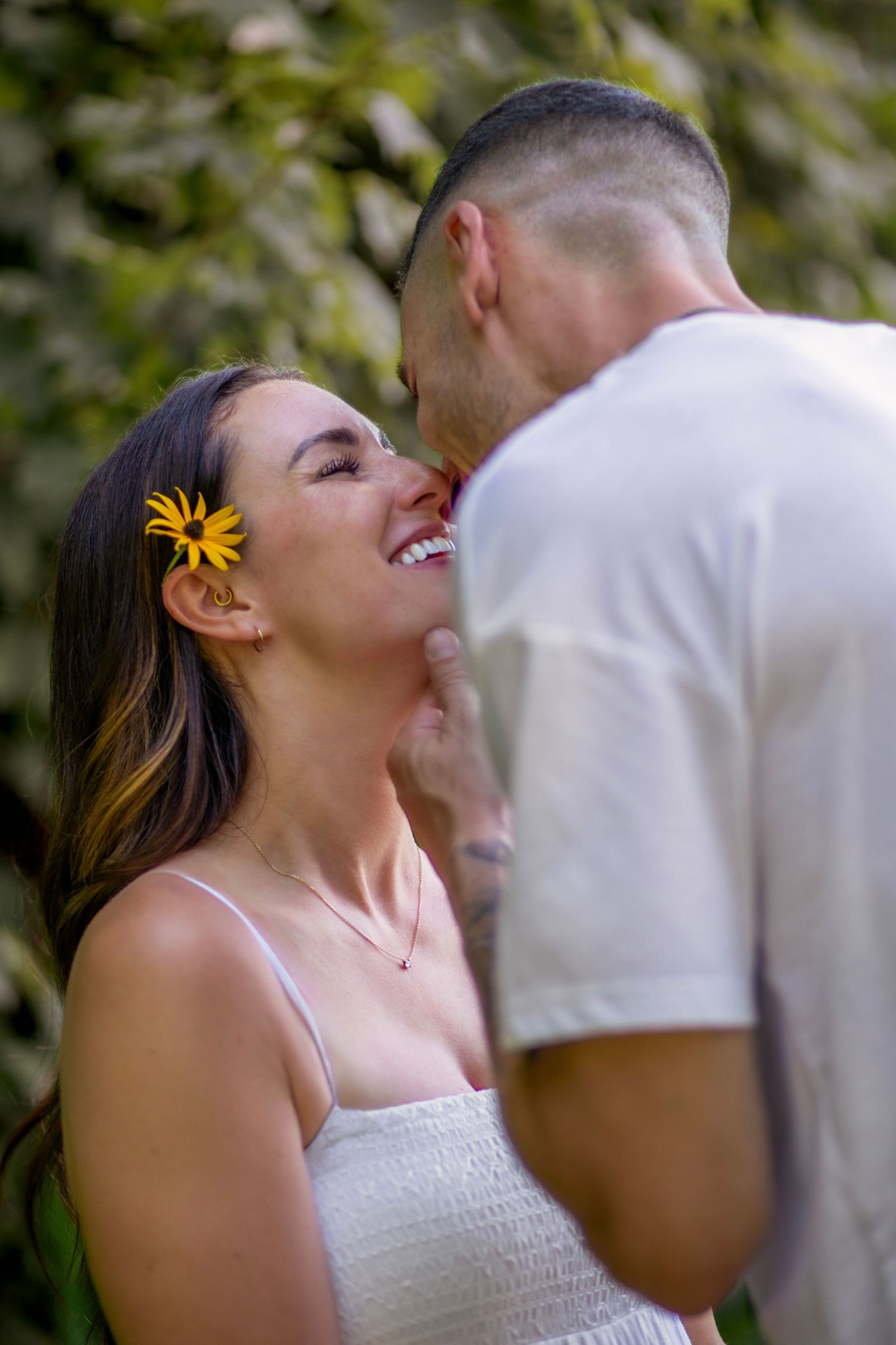 A joyful couple shares an intimate moment outdoors with a yellow flower accent in her hair.