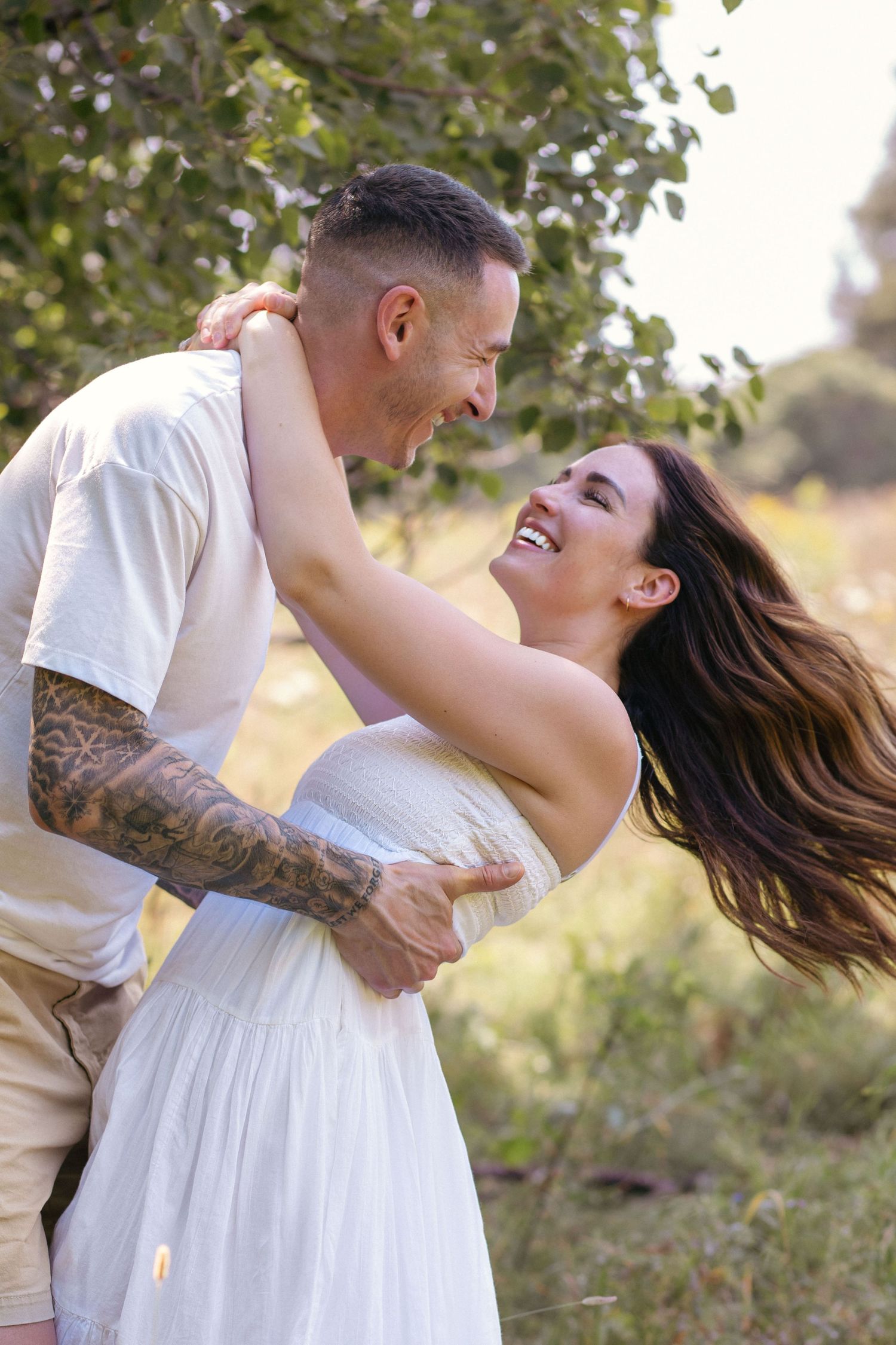 Dancing couple twirls joyfully in a sun-drenched field surrounded by tall grass and flowers.