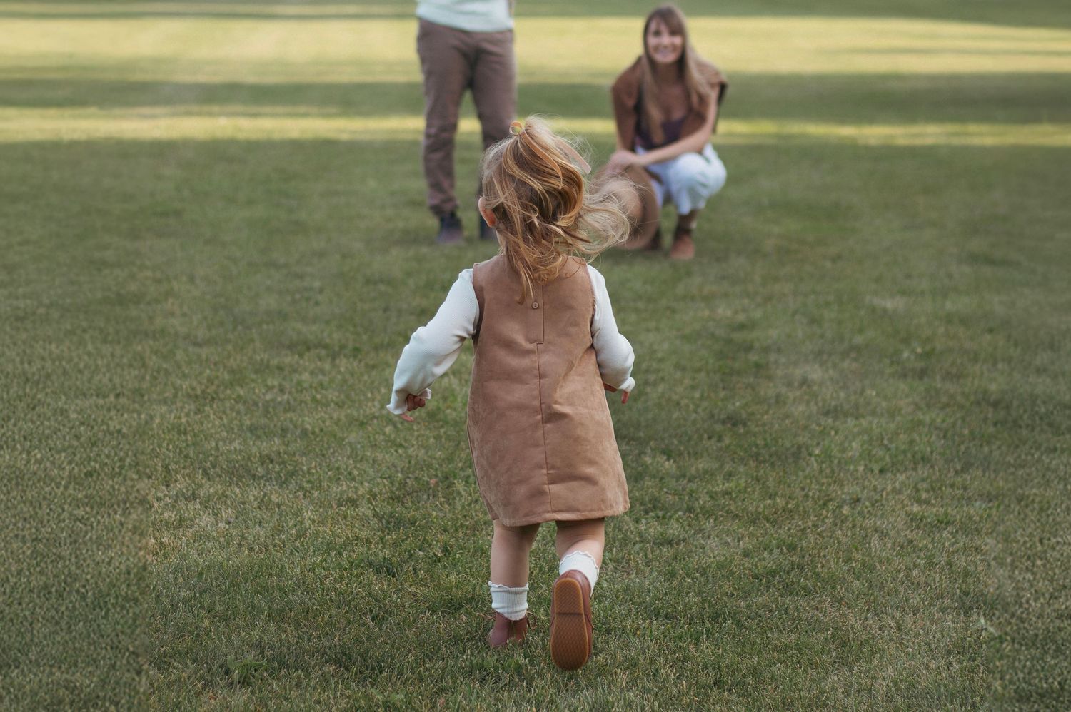 Happy family chasing and playing together across a green open field.