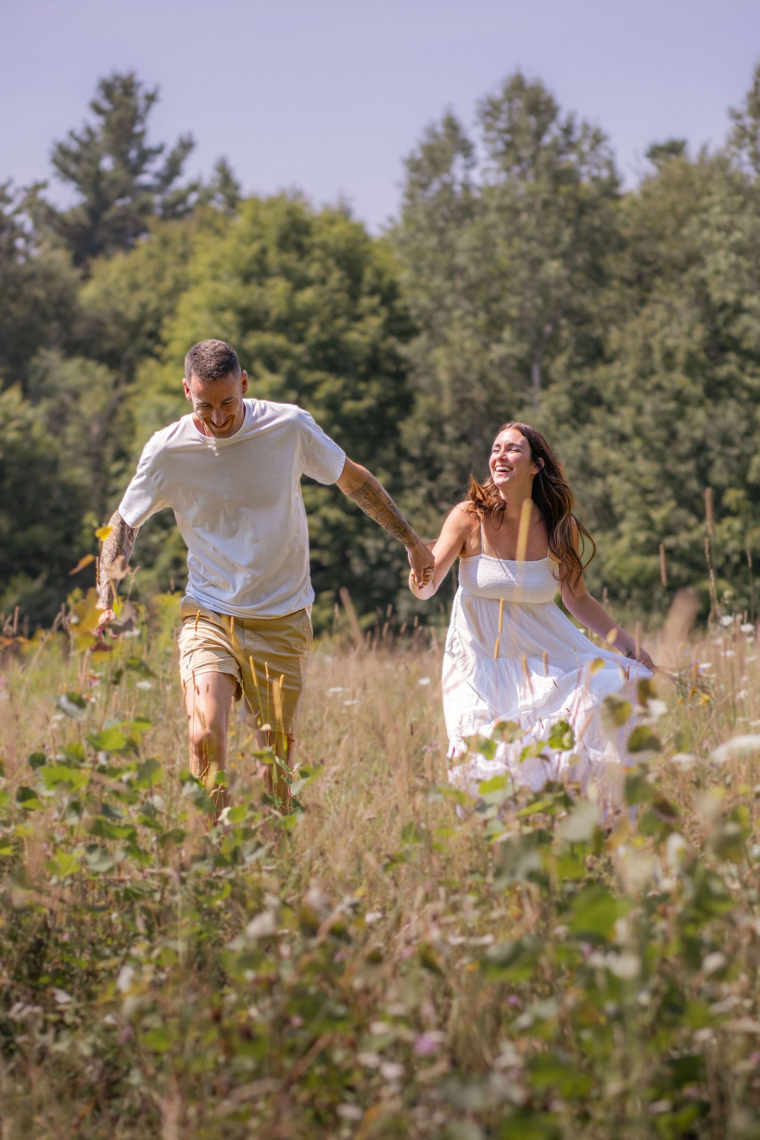 A couple dressed in white plays and laughs while running through a summer meadow.