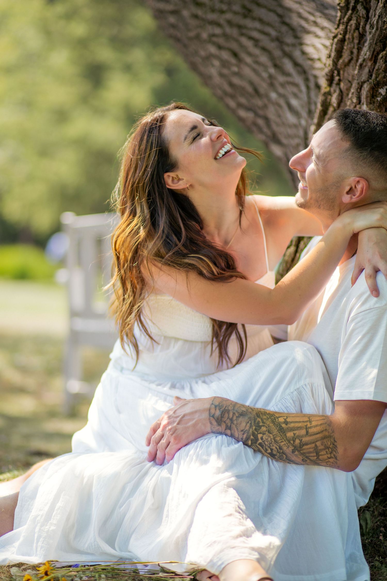 A couple shares joyful laughter during an intimate outdoor photo session near a tree.