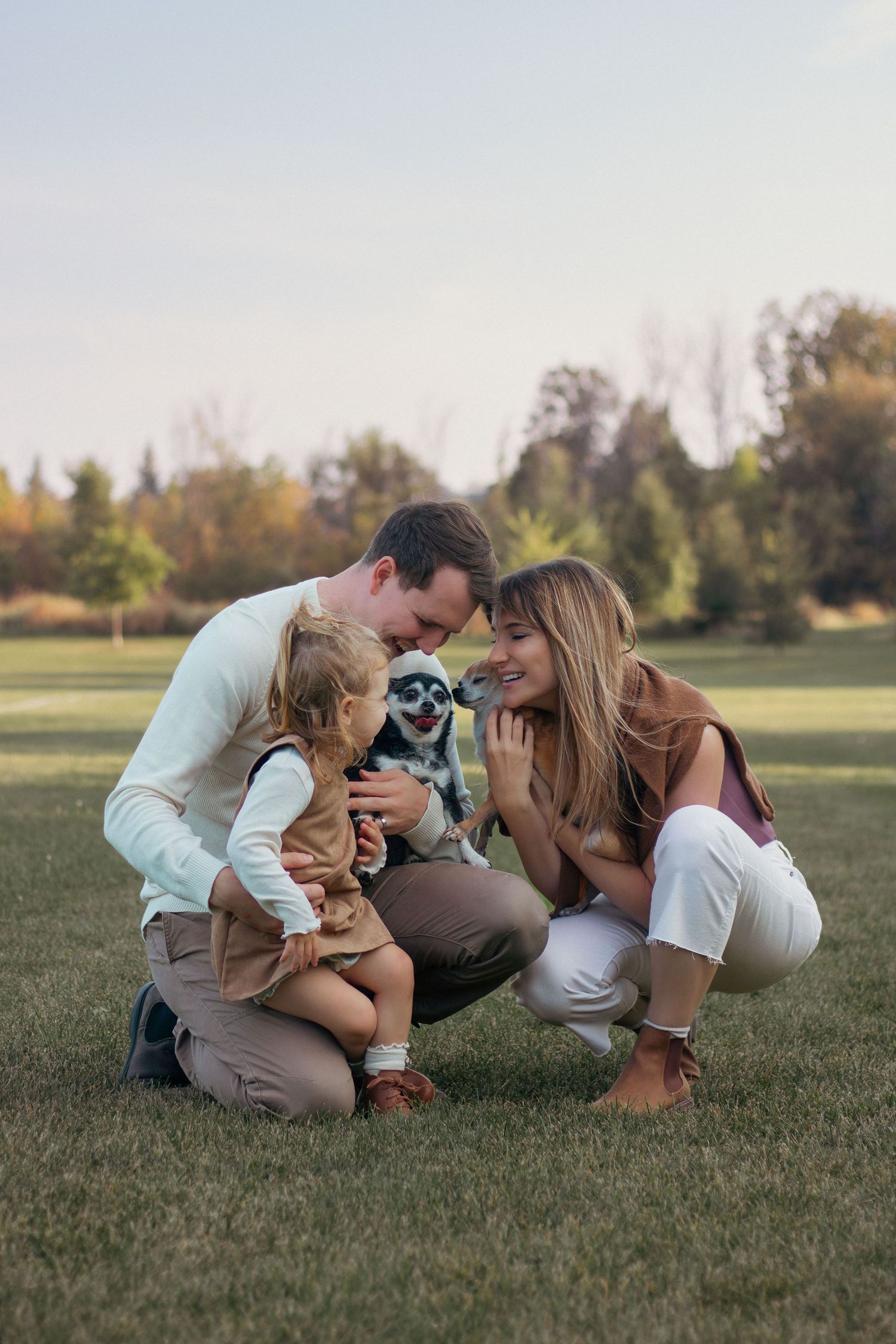 Family and dog sharing intimate moments while sitting on grass in a park setting.