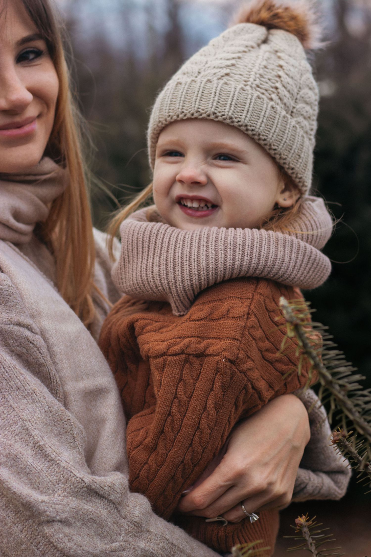 Joyful winter moments with knit beanies and brown cable knit sweater among pine trees.