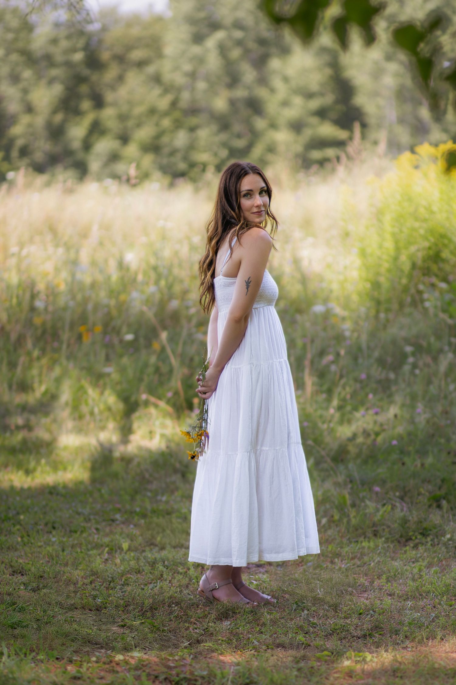 Woman in white dress explores a wildflower meadow during golden hour.