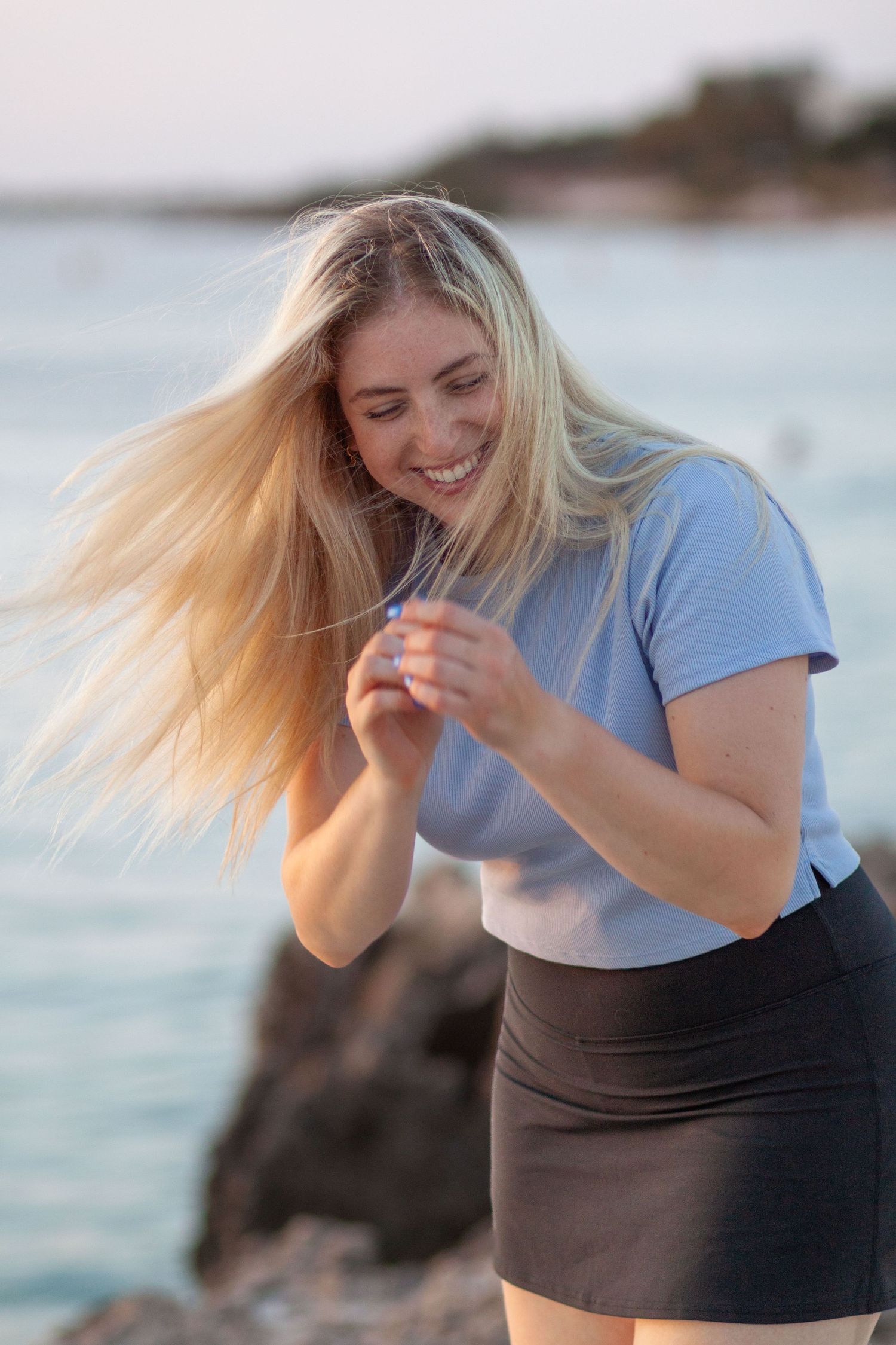 A sequence shows a woman in a blue shirt and black shorts laughing while enjoying time at the beach.