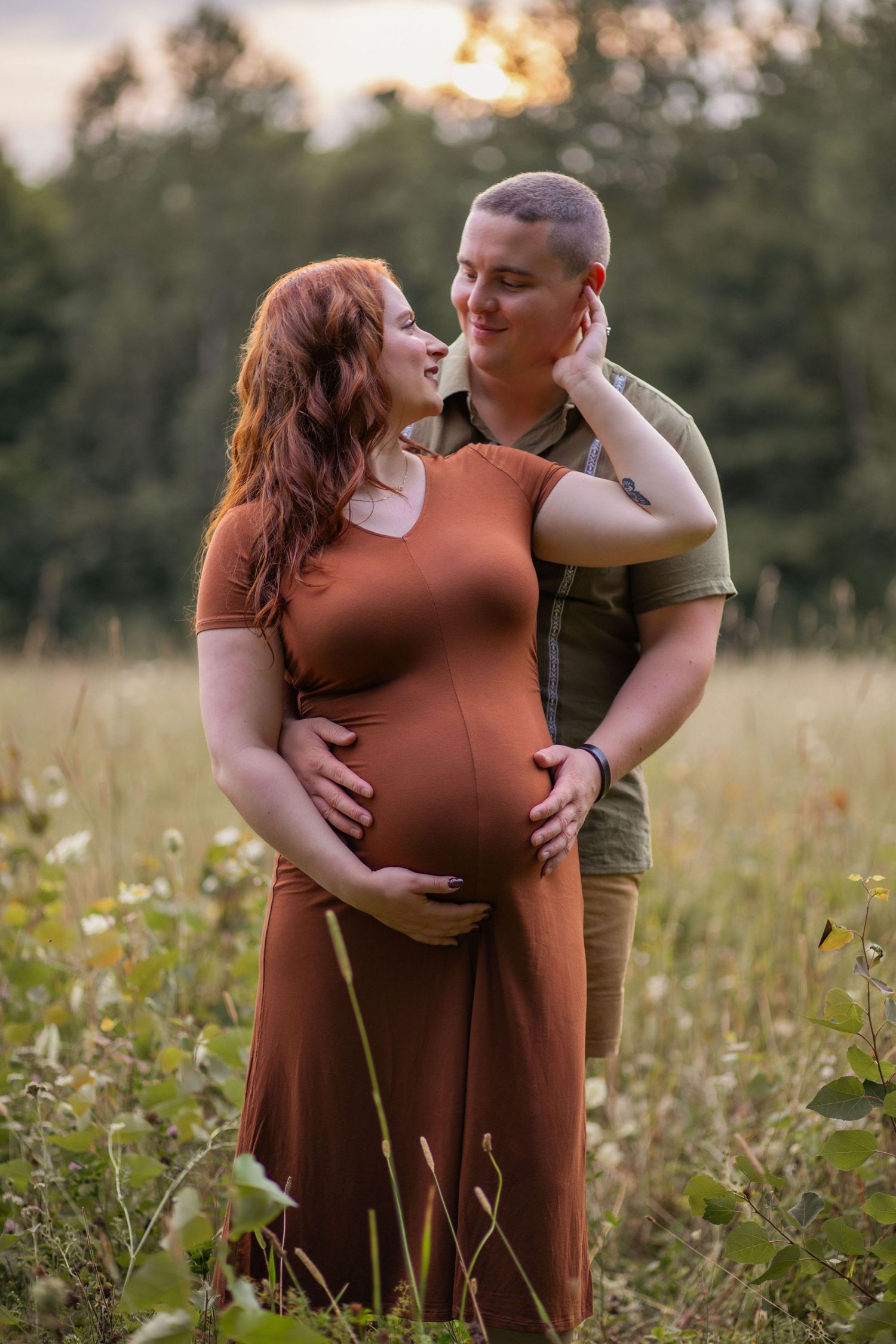 A couple shares a tender moment during their outdoor maternity photoshoot among tall grass and flowers.