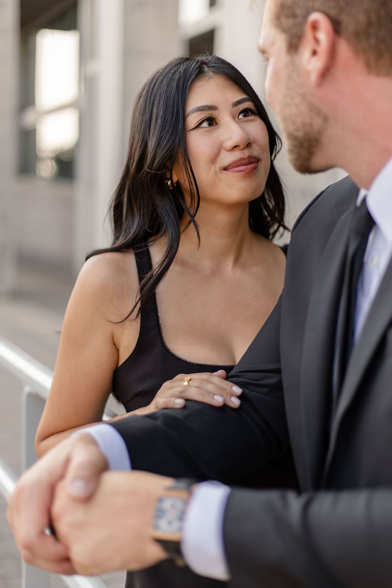 Couple in formal wear sharing affectionate moments against architectural backdrop.
