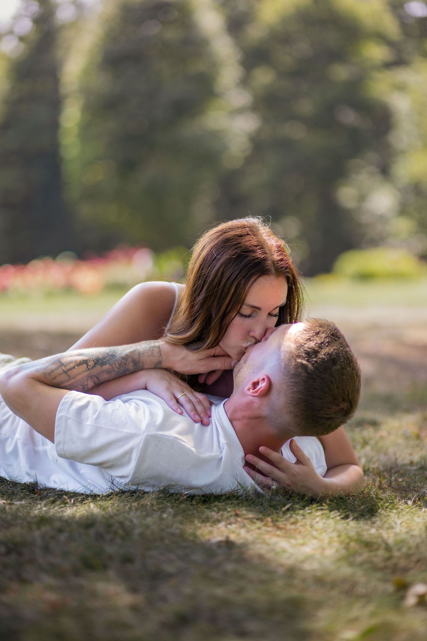 Tender moment between couple lying in grass wearing white clothes during outdoor photoshoot.