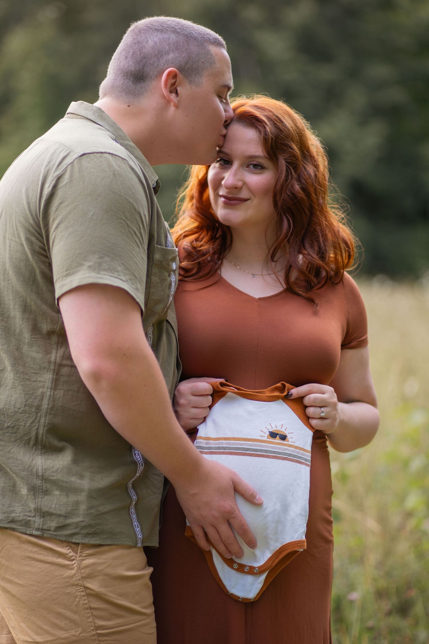 Couple reveals baby onesie during sunset pregnancy announcement session.