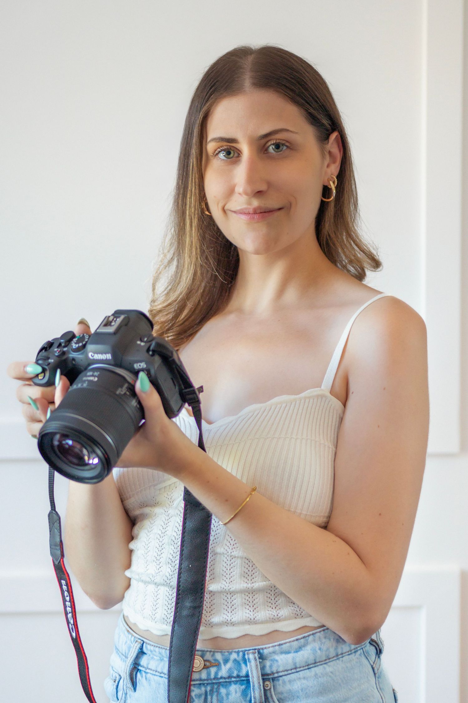 Woman in white tank top holds and demonstrates professional camera gear against bright indoor background.