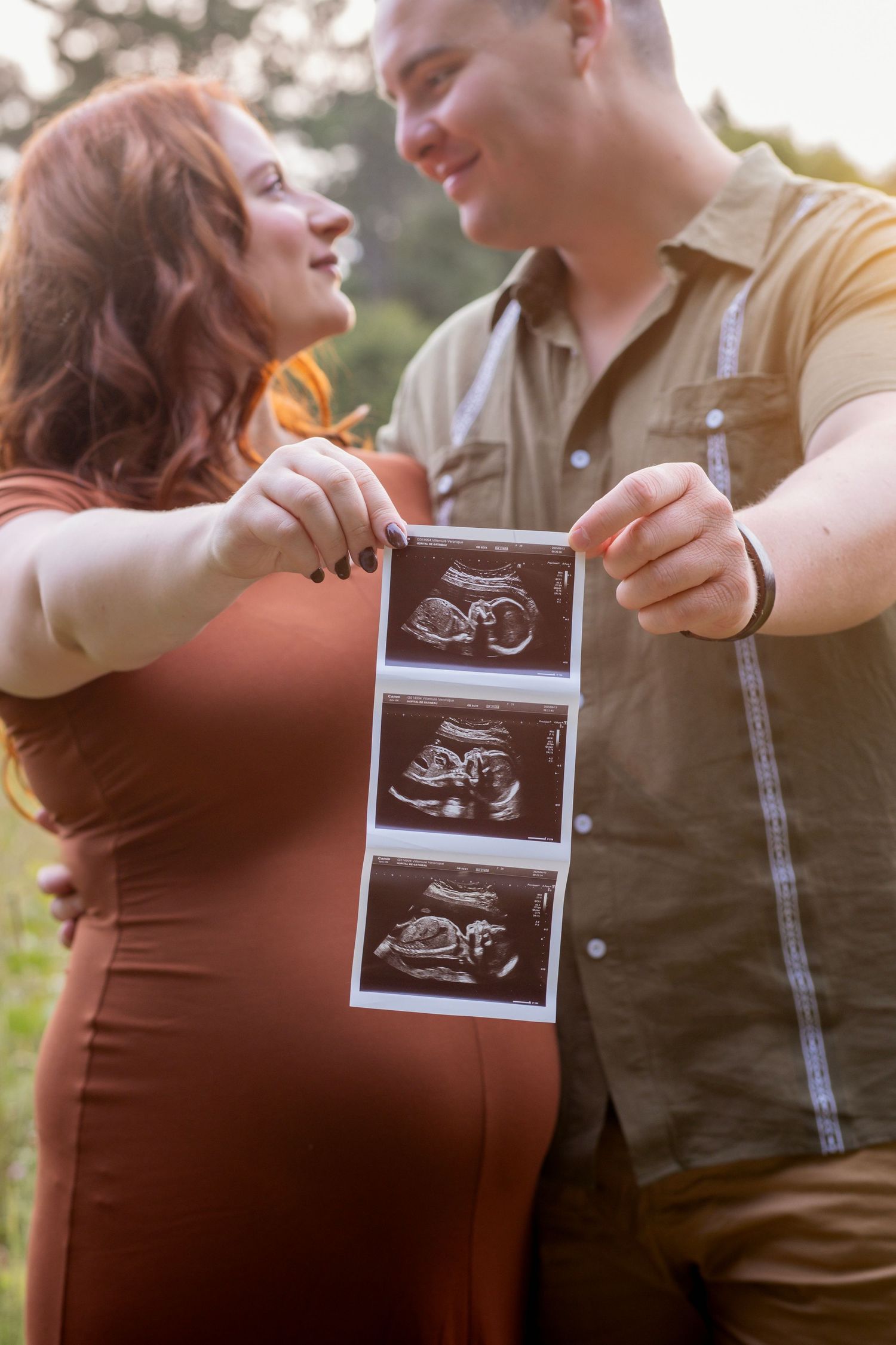 Couple shares emotional pregnancy announcement with sonogram photos in outdoor setting.